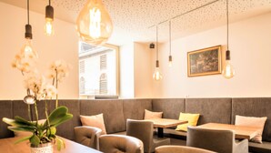 En restaurantindretning med siddepladser i båse, hængende lamper og en potteplante.