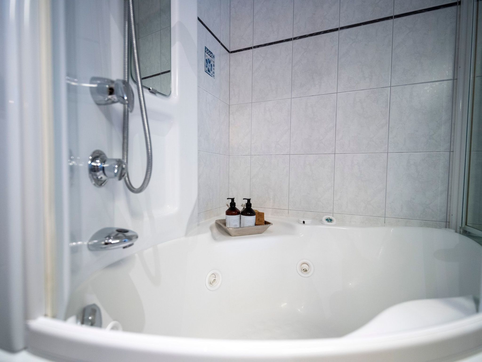 Un baño moderno con una bañera blanca, ducha y un pequeño recipiente con artículos de aseo.