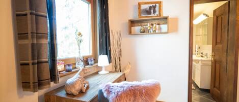 Um quarto acolhedor com uma escrivaninha de madeira, uma cadeira com manta de pele, uma janela com cortinas e uma prateleira com objetos decorativos.