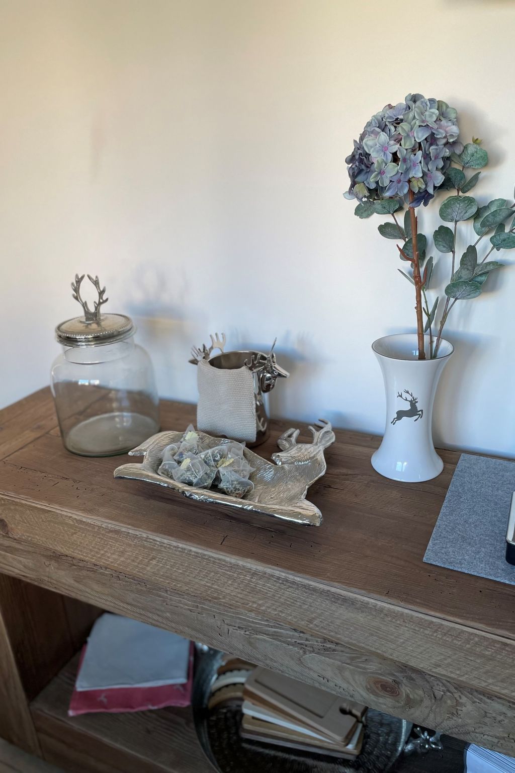 Et træbord med et glas, en keramik beholder med bestik, en dekorativ tallerken og en potteplante.