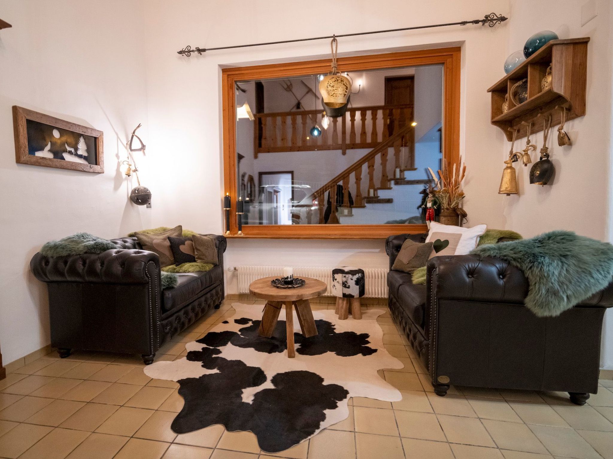 Ein Wohnzimmer mit zwei Ledersofas, einem Kuhfellteppich, einem runden Holztisch und einem großen Spiegel, der eine Treppe reflektiert.