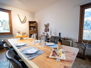 A dining area with a long table set for four, including plates, cutlery, glasses, and a bottle of wine. - Meis Chalet, (Scuol) by Interhome (Scuol)
