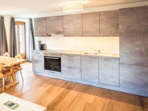 Eine moderne Küche mit grauen Schränken, einem eingebauten Ofen und einem Holztisch.