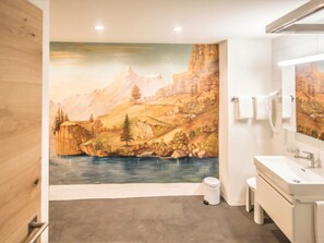 Ein Badezimmer mit einer Wandmalerei einer Berglandschaft, einem Waschbecken und einem Spiegel.