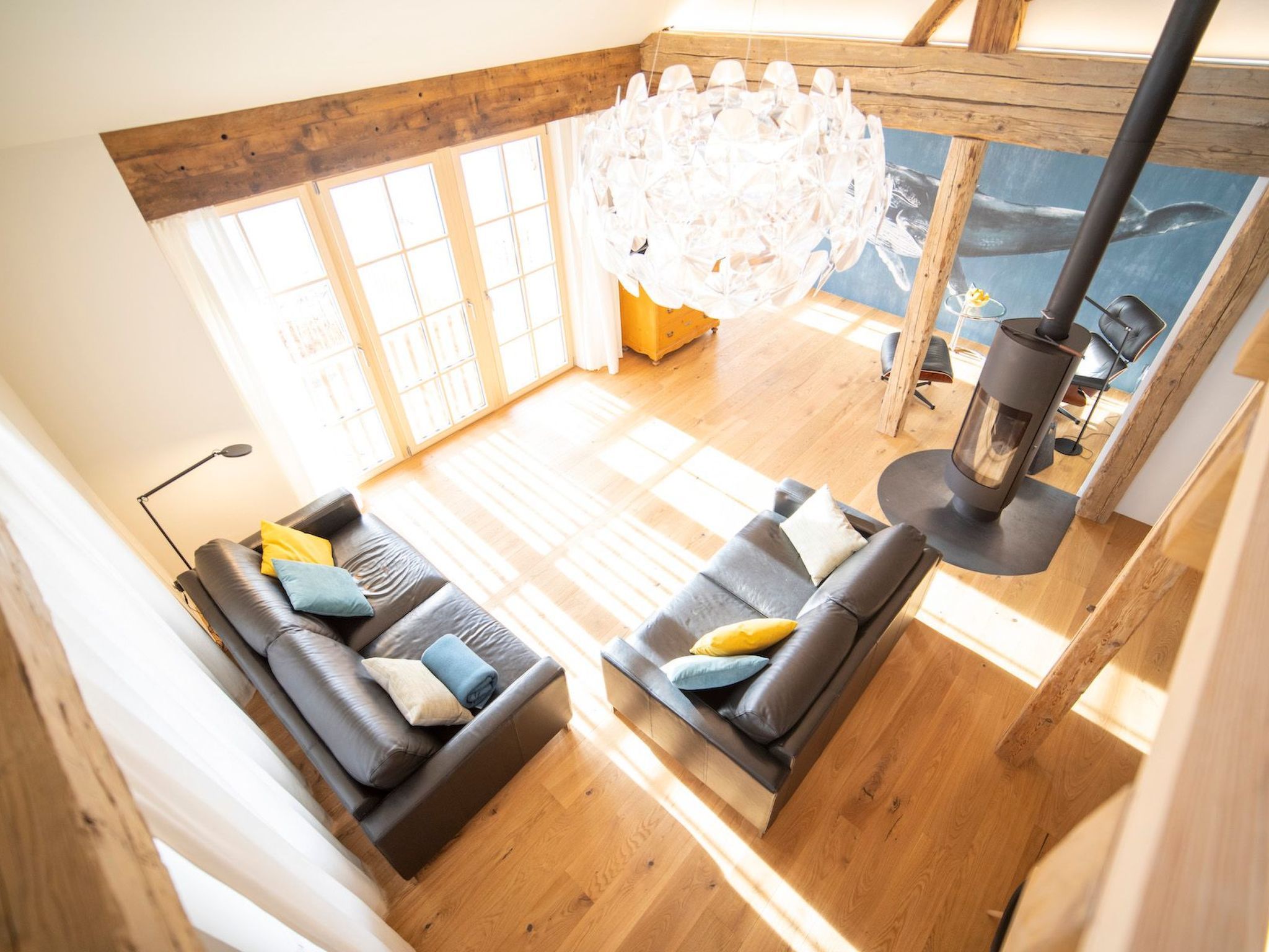 A spacious room with a large window, a modern chandelier, and a fireplace.