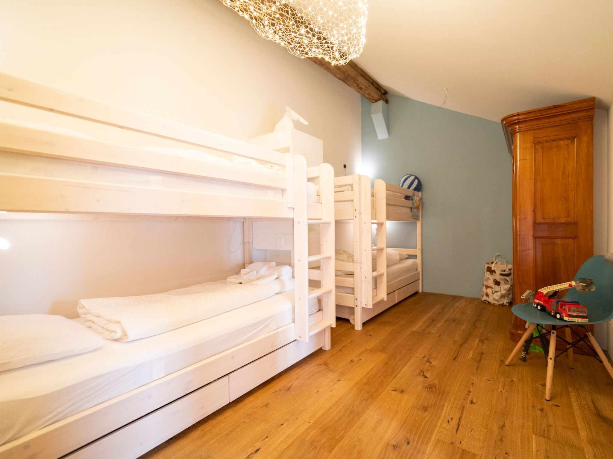 Une pièce avec des lits superposés, une armoire en bois, une chaise et un luminaire au plafond.