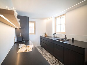 A modern kitchen with a dark countertop, a coffee machine, a sink, and a window. - Chasa Muntanella, (Ftan) by Interhome (Ftan)