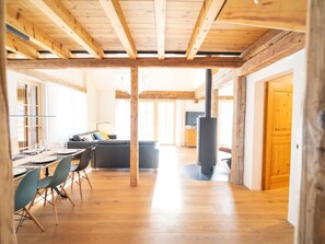 A spacious living area with a wooden ceiling, a sofa, a dining table with chairs, and a fireplace. - Chasa Muntanella, (Ftan) by Interhome (Ftan)