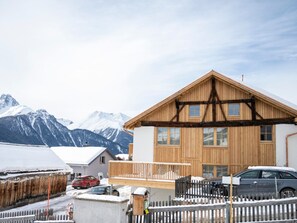 A wooden chalet with a balcony, surrounded by a white picket fence, set against a backdrop of snow-covered mountains. - Chasa Muntanella, (Ftan) by Interhome (Ftan)