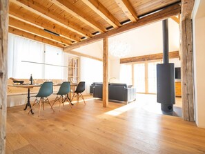 A spacious living area with wooden beams, a dining table with chairs, a sofa, and a fireplace. - Chasa Muntanella, (Ftan) by Interhome (Ftan)