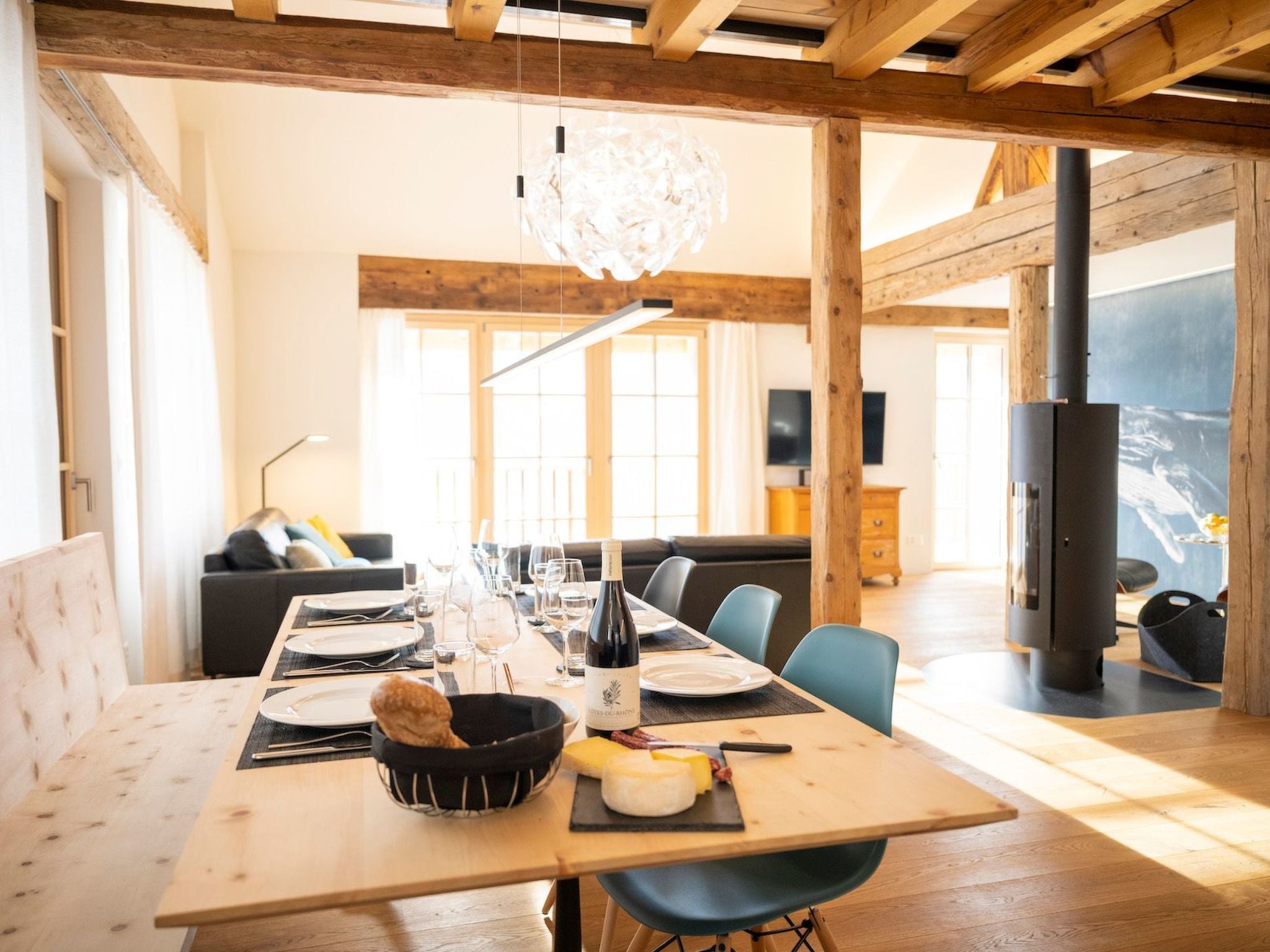 A dining area with a long table set for a meal, wooden beams on the ceiling, and a large window providing natural light.