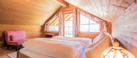 A cozy wooden cabin bedroom with a bed, a chair, and a lamp.