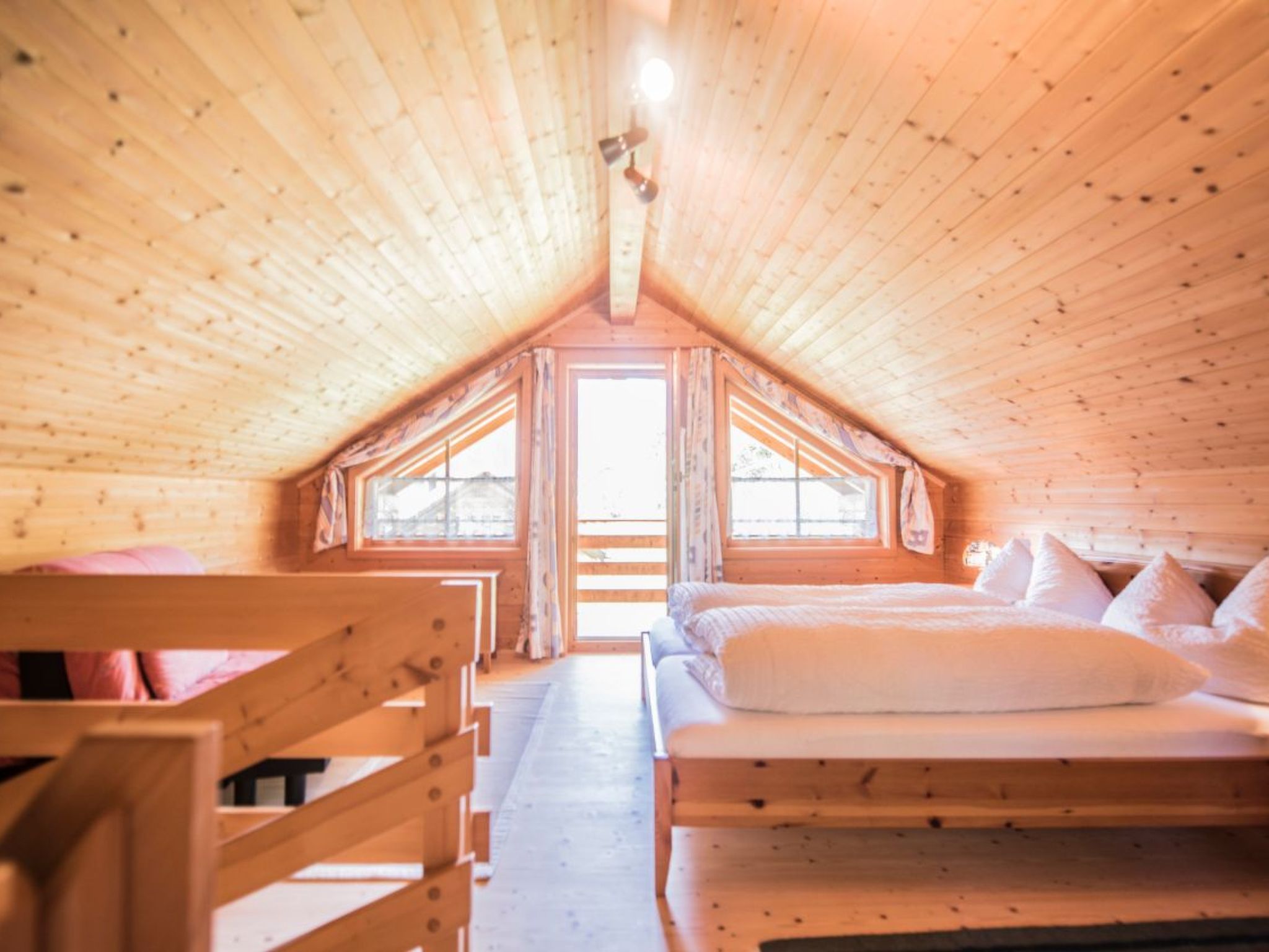 A wooden attic bedroom with a sloped ceiling, a bed, a window, and a view of the outside.