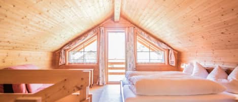 Un dormitorio de madera en el ático, con techo inclinado, una cama, un ventanal y vistas al exterior.