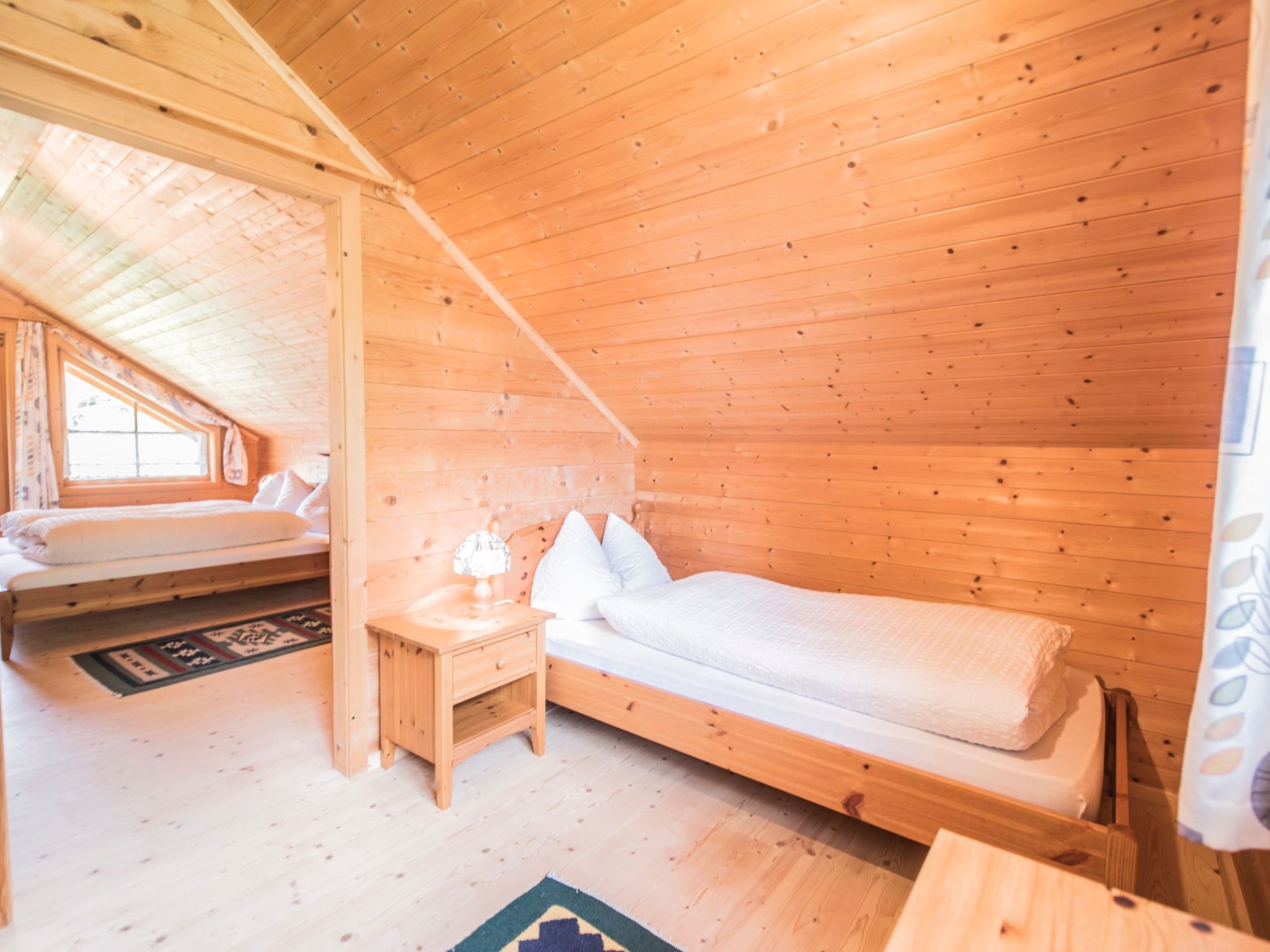 Habitació de cabana de fusta amb un llit amb altell, una taula de nit amb una làmpada i una finestra.