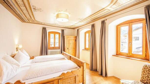 Ein Zimmer mit einem Bett, einem Holzschrank, einem Stuhl und einem Vorhangfenster.