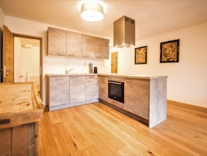 A modern kitchen with wooden flooring, built-in cabinets, a stainless steel range hood, and a dishwasher.
