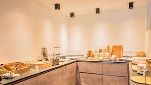 Eine moderne Frühstückslounge mit vielfältigen Speisen und Getränken, darunter Gläser, Schalen und eine Kaffeemaschine.
