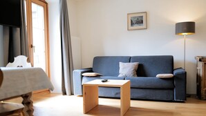 Ein Wohnzimmer mit einer Couch, einem kleinen Holztisch, einer Lampe und einem gerahmten Bild an der Wand.