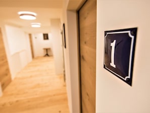 Un pasillo con suelo de madera, un cartel con número en la pared y luces empotradas en el techo.