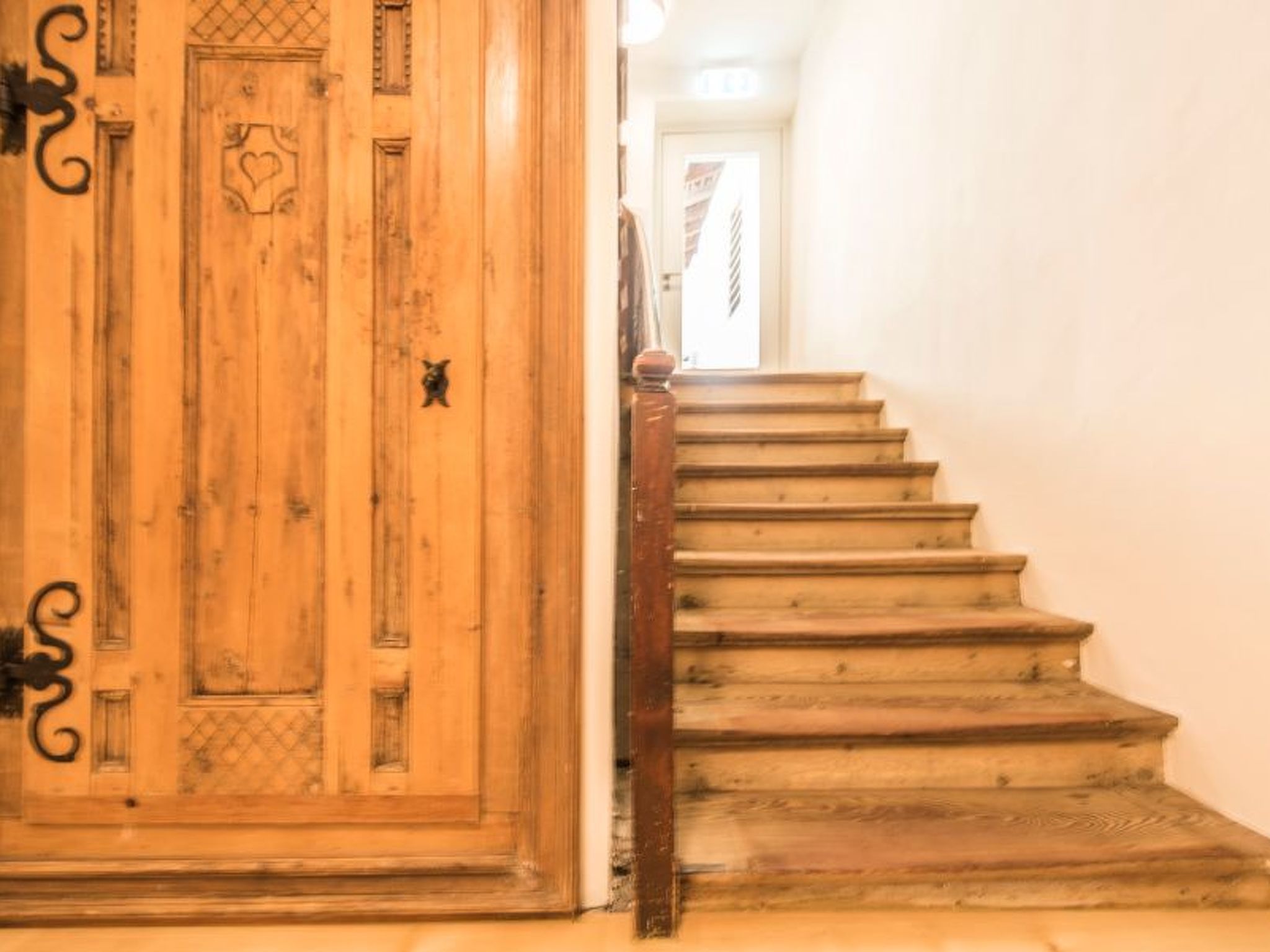 Una escalera de madera con barandilla que conduce a una puerta con diseño de corazón.