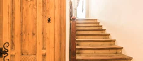 Un escalier en bois, doté d’une rampe, mène à une porte ornée d’un motif en forme de cœur.