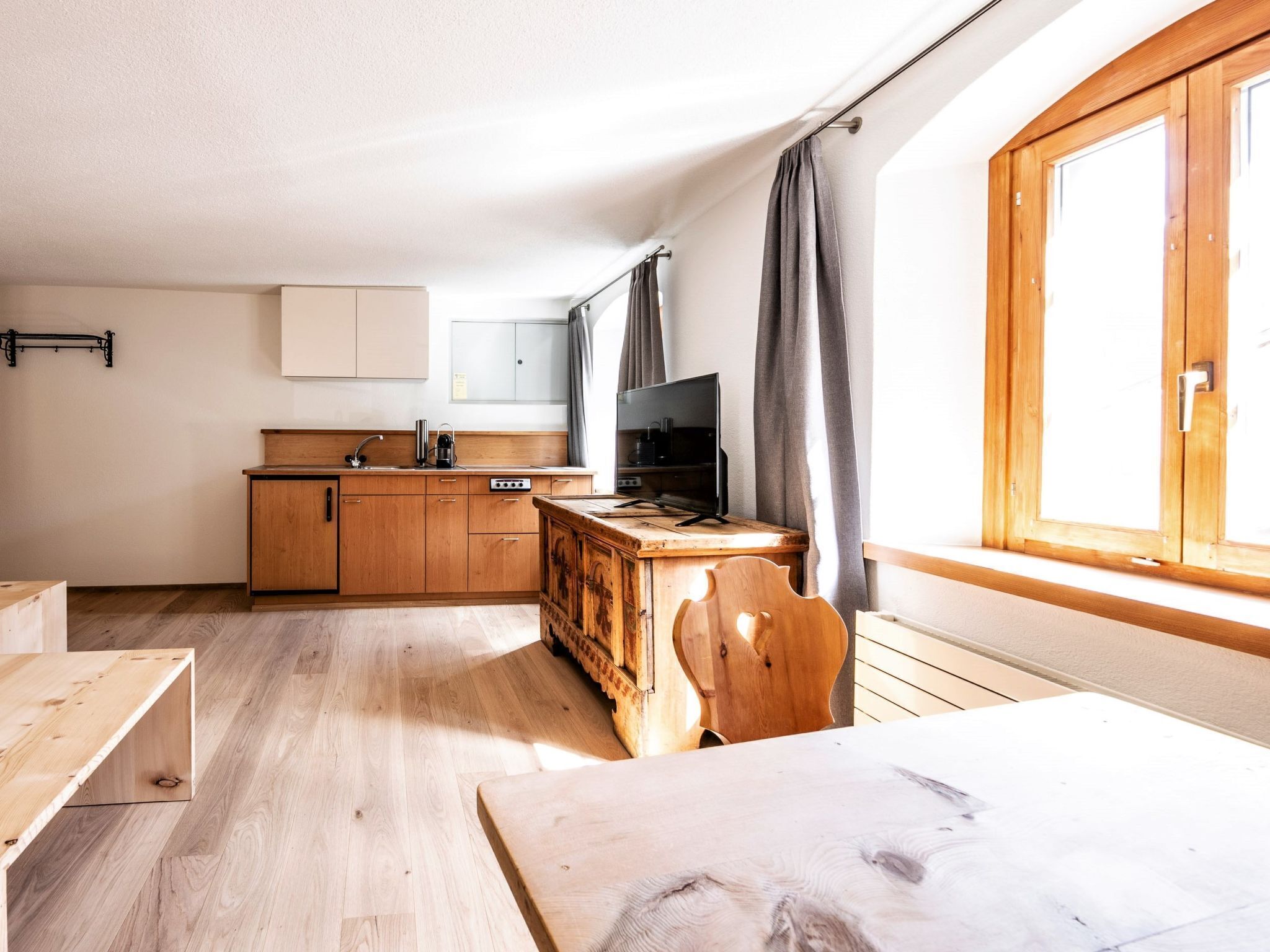 A compact kitchen with wooden cabinets, a built-in stove, and a dining area with a wooden table and bench.