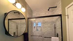 Ein modernes Badezimmer mit einer Duschkabine aus Glas, einem runden Spiegel und einem weißen Waschbecken.