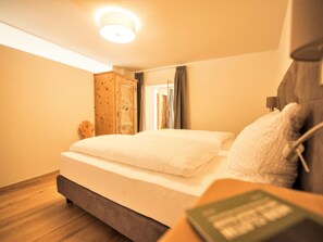 Un dormitorio con cama, un armario de madera, una mesita de noche con lámpara y vistas a un pasillo.