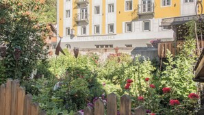 Un bâtiment jaune doté de nombreuses fenêtres et de balcons, entouré d’un jardin où poussent différentes plantes et fleurs.
