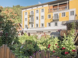 A yellow building with multiple windows and balconies, surrounded by a garden with various plants and flowers.