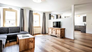Ein modernes Wohnzimmer mit einer Couch, einem Couchtisch, einem Fernseher auf einem Holzschrank und Blick auf eine Küche.