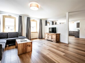 A modern living room with a sofa, a coffee table, a TV on a wooden cabinet, and a view of a kitchen. - Appartements Münsterhof, (Müstair) by Interhome (Müstair)