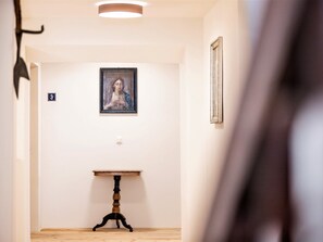 A hallway with a framed artwork on the wall, a small table, and a door with a number sign. - Appartements Münsterhof, (Müstair) by Interhome (Müstair)