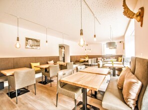 Een restaurantinterieur met zitjes, tafels, hangende lampen en een aan de muur bevestigd vogelbeeld.