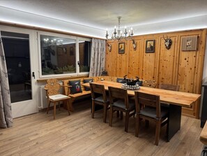A dining area with a wooden table and chairs, a chandelier, and deer antlers on the wall. - Berg-Bijou Scuol, (Scuol) by Interhome (Scuol)