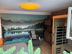 A room with a mountain landscape mural, a chair, a wooden cabinet, and a glass door. - Berg-Bijou Scuol, (Scuol) by Interhome (Scuol)