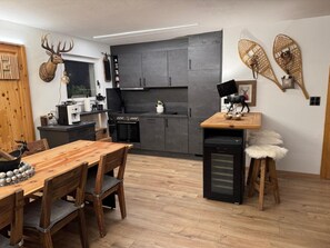 Una cocina moderna con armarios oscuros, una mesa de comedor de madera y un refrigerador pequeño.