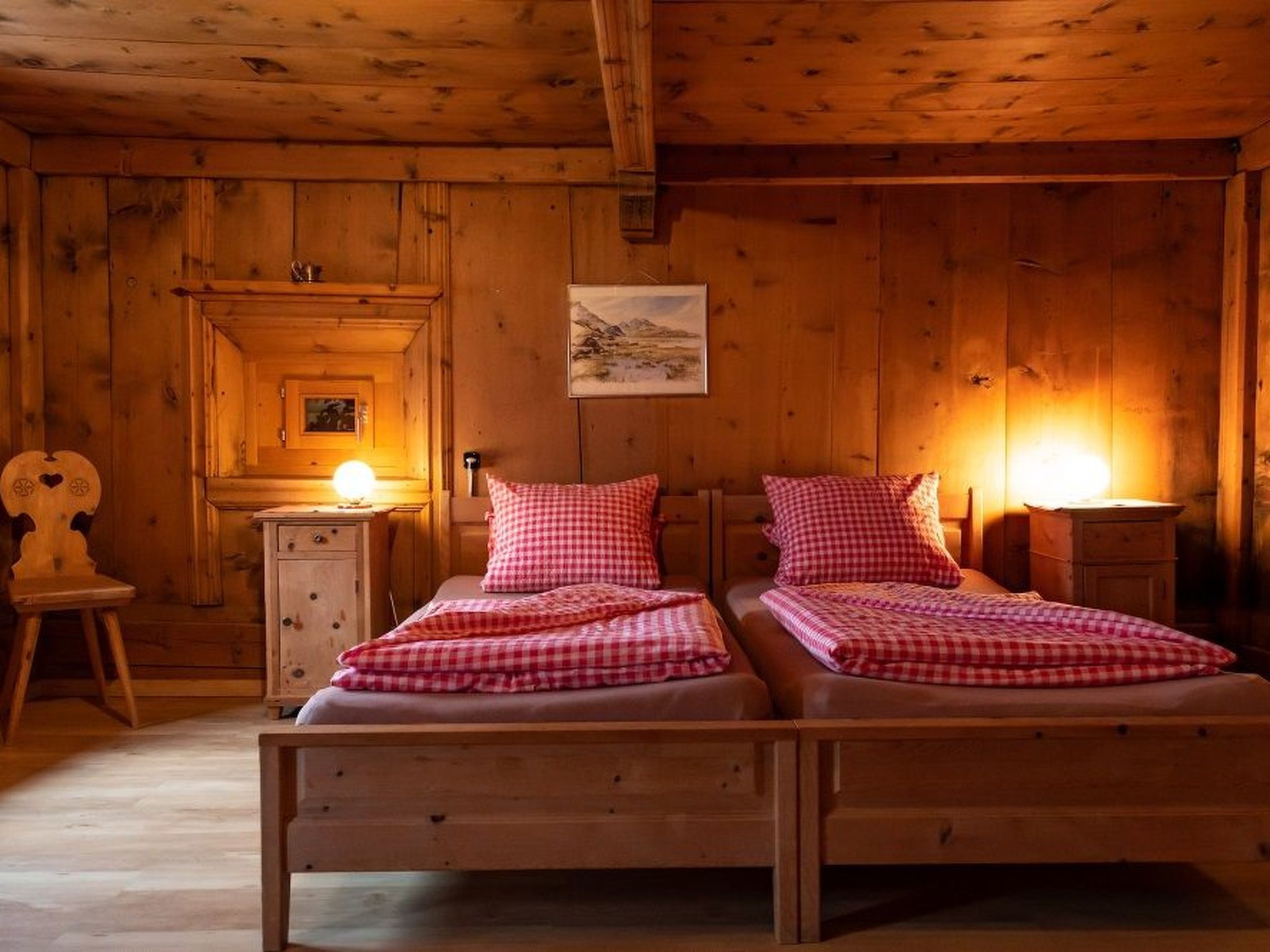 Une chambre dans un chalet en bois, avec deux lits, une armoire en bois et un tableau accroché au mur.