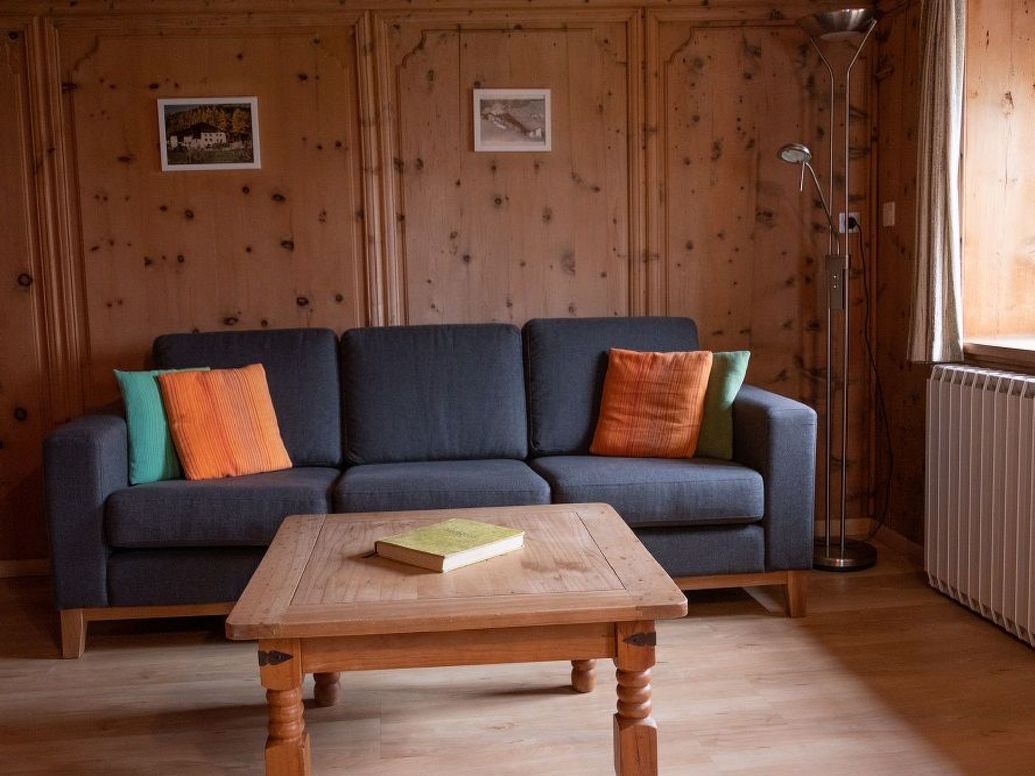 A room with a dark blue sofa, two colorful cushions, a wooden coffee table with a book, and a floor lamp.