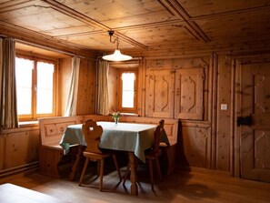 Comedor de madera con una mesa dispuesta para cuatro, una araña y ventanas amplias.