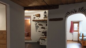 A room with a stone wall, wooden beams, a bed with a checkered bedspread, and a window with a pink curtain. - Agrotourismus Pütschai Josom, (Sta. Maria - Santa Maria Val Müstair) by Interhome (Sta. Maria GR)