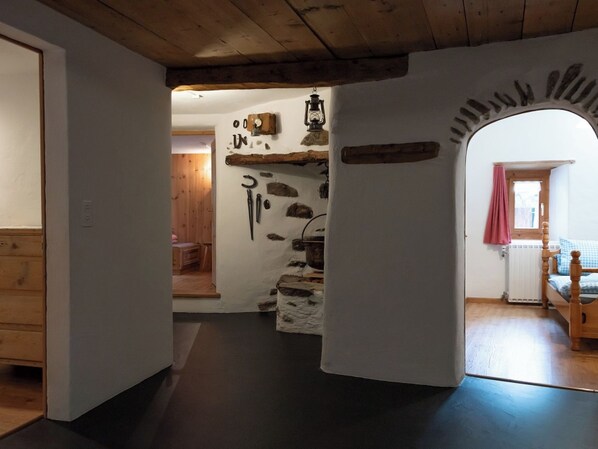 Una habitación con pared de piedra, vigas de madera, cama con colcha a cuadros y ventana con cortina rosa.