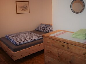 A single bed with a checkered bedspread, a wooden dresser with a mirror, and a framed picture on the wall.