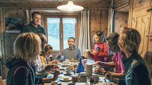 A group of people dining in a wooden cabin with a table set for a meal, a window with curtains, and a hanging light fixture. - Agrotourismus Pütschai Josom, (Sta. Maria - Santa Maria Val Müstair) by Interhome (Sta. Maria GR)