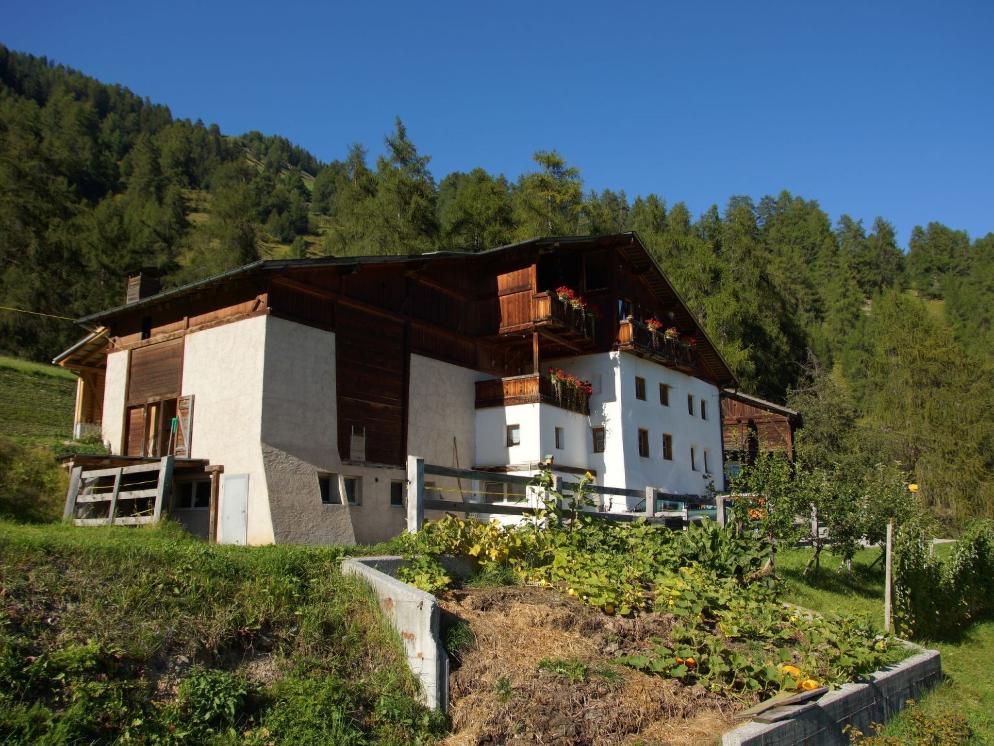 Un chalet à deux étages, doté d’un toit en pente, entouré d’un jardin luxuriant et de collines boisées.