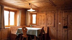 A wooden dining room with a table set for four, a hanging light fixture, and a window with curtains. - Agrotourismus Pütschai Josom, (Sta. Maria - Santa Maria Val Müstair) by Interhome (Sta. Maria GR)