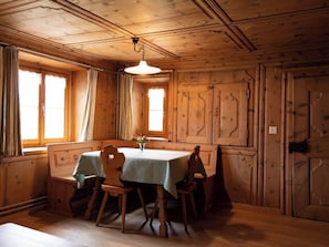 Un comedor de madera con una mesa preparada para cuatro, una lámpara colgante y un ventanal con cortinas.
