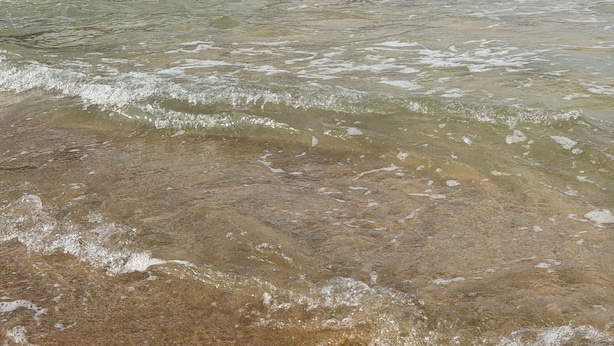 Una zona costiera con acque limpide, una spiaggia e una collina con edifici.