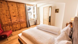 Ein Schlafzimmer mit einem Holzschrank, einem roten Sessel, einem Bett mit weißer Bettwäsche und einem Fenster mit Blick.